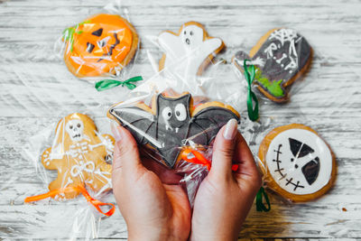 Cropped hands of woman holding various cookies wrapped in plastic over wooden table during halloween