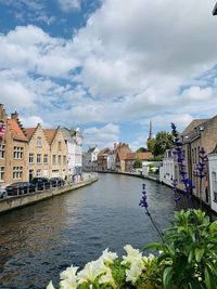 View of buildings by river against cloudy sky