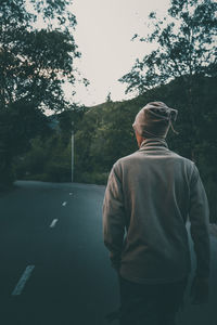 Rear view of man standing on road against trees