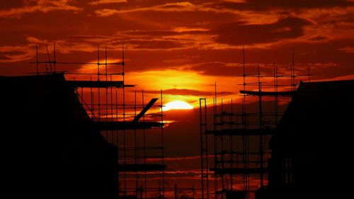 Silhouette cranes against sky during sunset