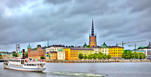 Buildings by river against cloudy sky