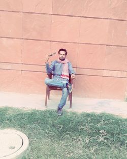 Portrait of man sitting on chair against wall
