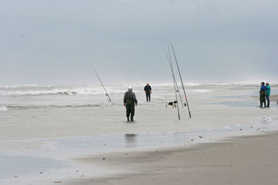 Men fishing on beach against clear sky