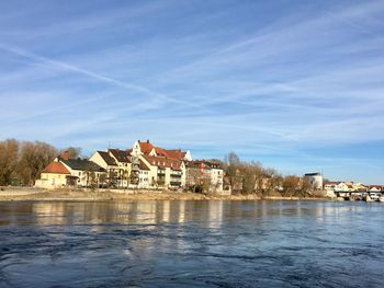 Buildings by river against blue sky