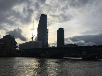 Modern buildings by river against sky in city