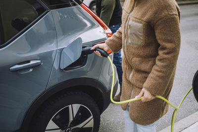 Midsection of woman charging electric car at station