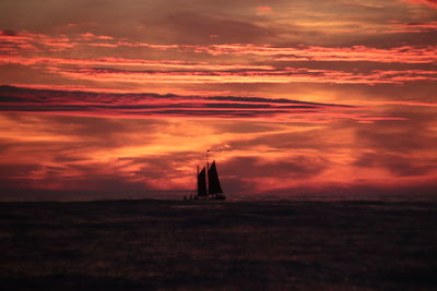 Silhouette sailboat sailing on sea against orange sky