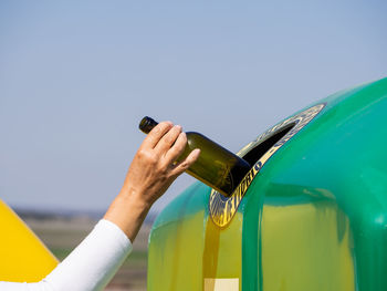 Midsection of person holding bottle against clear sky