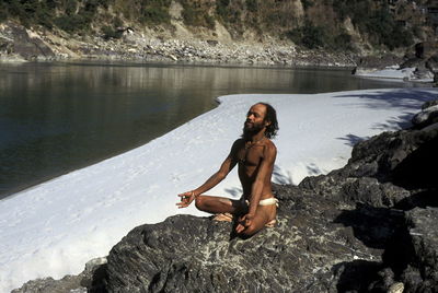 Man meditating on rock by frozen lake