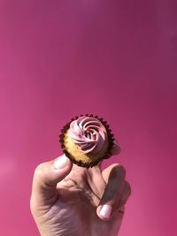 Cropped hand holding dessert against pink background