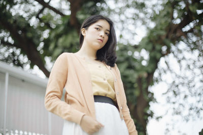 Portrait of young woman standing against trees