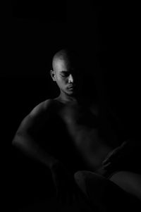 Shirtless young man looking away while sitting against black background