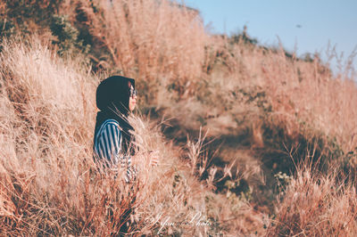 Side view of woman wearing hijab while standing on grassy field