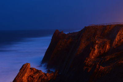 Scenic view of cliff by sea against clear blue sky