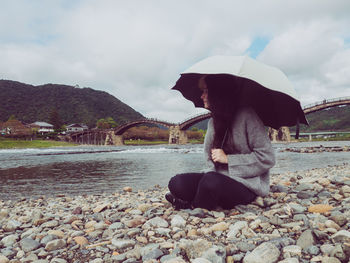 Man sitting on shore against sky