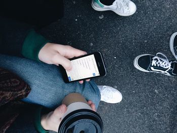 Low section of man with disposable coffee cup using mobile phone on street