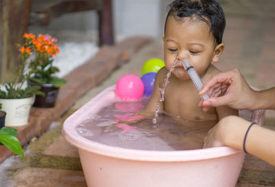 Cropped hand of woman cleaning baby nose using syringe at home