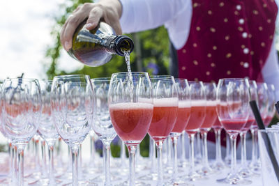 Midsection of bartender pouring aperitif in champagne flutes on table during outdoor party