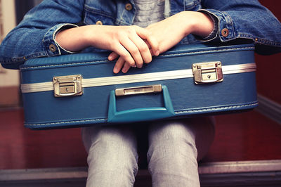 Close-up mid section of woman sitting with suitcase