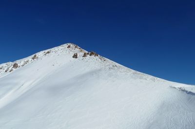 Low angle view of snowcapped mountain against clear blue sky