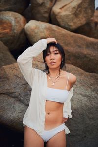 Portrait of sensuous young woman wearing bikini standing against rocks