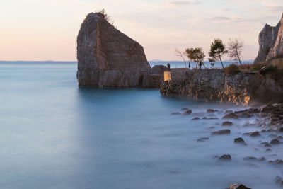 Rocks on sea shore against sky during sunset