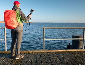 Photographer with red backpack on wooden pier above sea. touristic mole, wet wooden floor above sea.