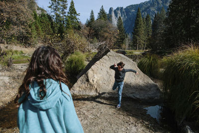 Rear view of sister looking at brother running by rock at yosemite national park in forest