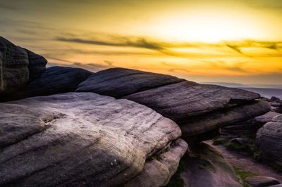 Rocks by sea against sky during sunset
