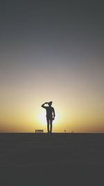 Silhouette man standing on beach against clear sky during sunset