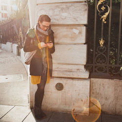 Full length of man holding mobile phone while standing against building