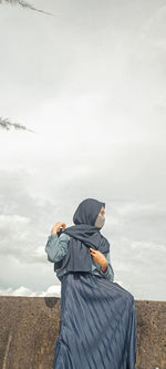 Low angle view of woman looking away while sitting against sky