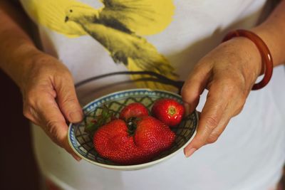 Midsection of woman holding strawberries in bowl