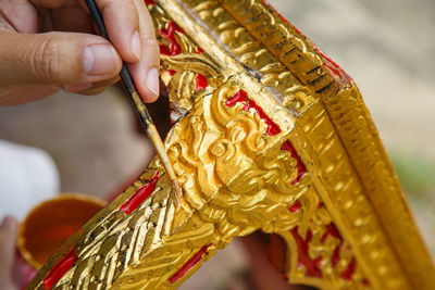 Close up a man's hand holding a brush is painting golden on the altar table