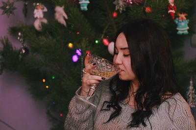 Young woman having drink while standing by christmas tree at home