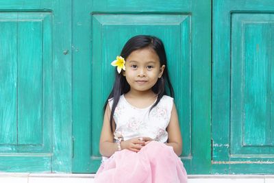 Portrait of cute girl wearing flower sitting against closed doors