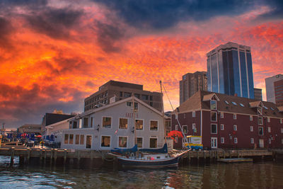 Boats moored in canal by buildings against sky during sunset