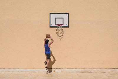 Man playing with basketball against beige wall