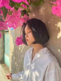 Side view of woman looking away against pink flowers on wall