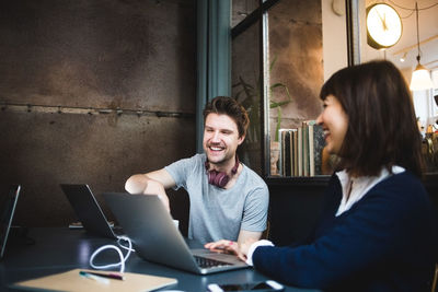 Cheerful female and male entrepreneurs discussing over laptop at desk in office