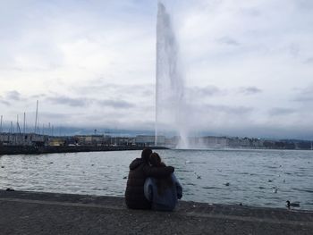 Rear view of people sitting on bridge against cloudy sky