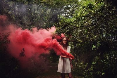 Portrait of woman holding distress flare while standing by trees