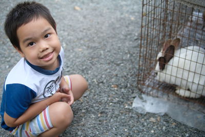 Portrait of smiling boy crouching by rabbit in cage