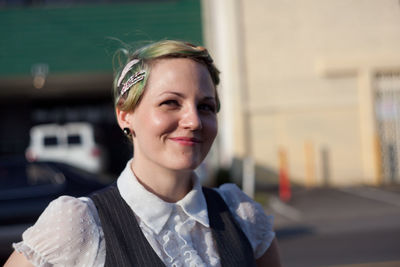 Portrait of smiling young woman in city against sky