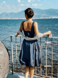 Rear view of woman standing on railing against sea