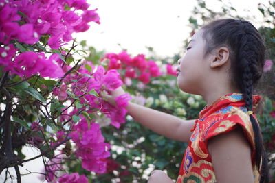 Low angle view of girl by pink flowering plants against sky