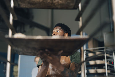 Male baker removing tray from cooling rack while working at bakery