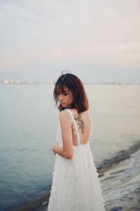 Young woman standing by sea against sky