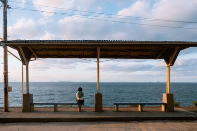 Rear view of thoughtful mid adult woman looking at sea against cloudy sky