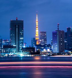 Light trails on illuminated buildings against sky at night